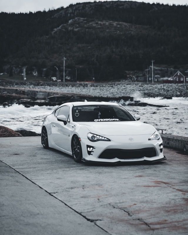 A white Toyota GT86 parked on a concrete slipway beside a rocky coastline
