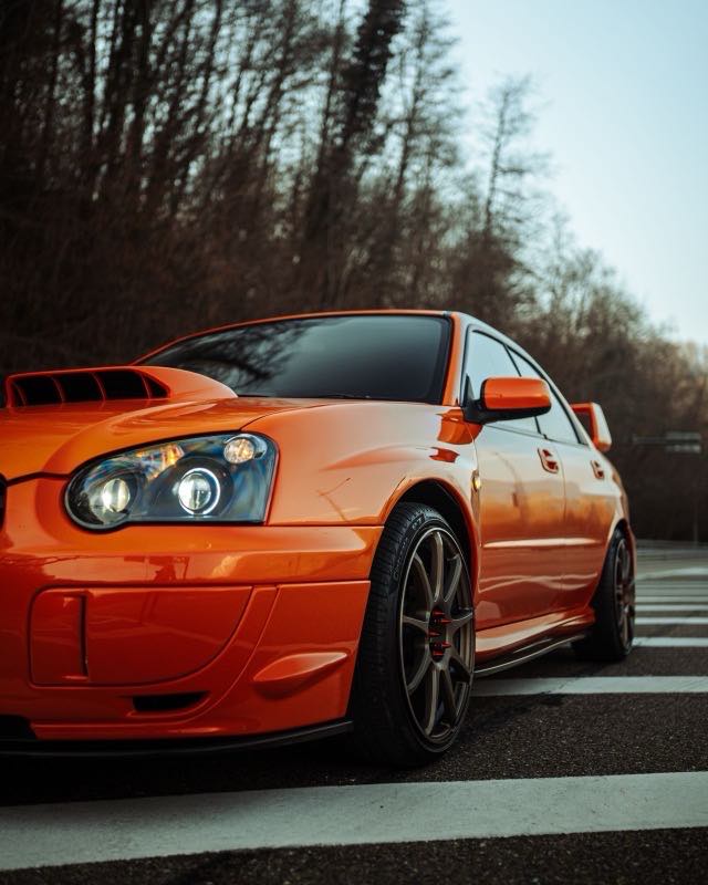 An orange Subaru Impreza WRX shot low from the front left on a marked road