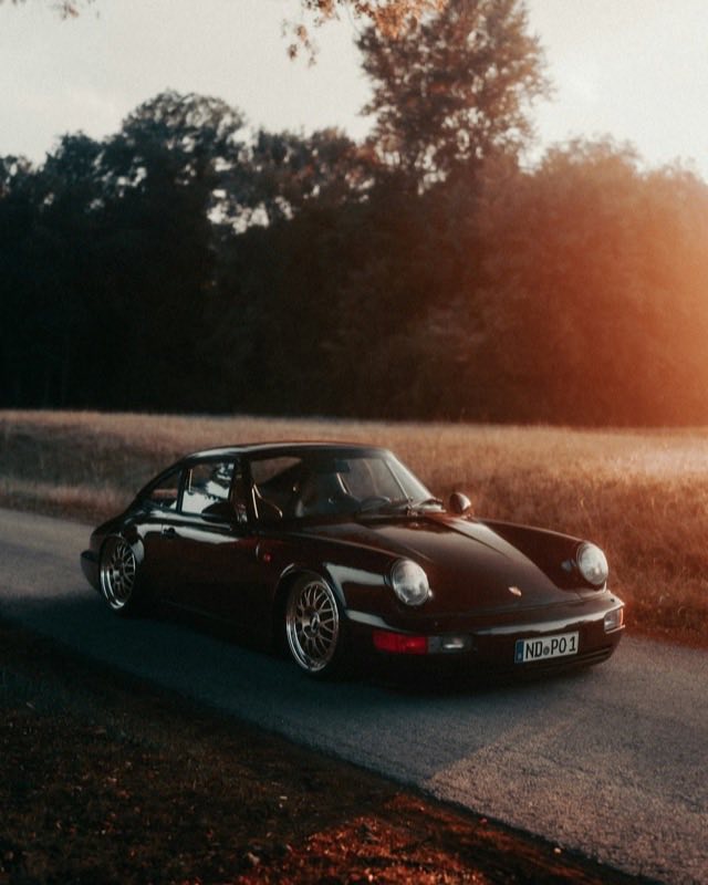 A dark Porsche 911 964 parked on a country road in low sunset light