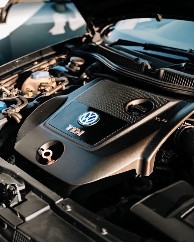 A Volkswagen four-cylinder diesel engine under an open bonnet, its plastic cover carrying a TDI badge