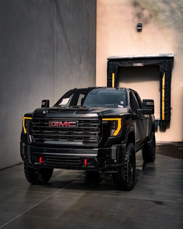 A black GMC Sierra HD crew cab pickup parked on wet concrete beside an industrial loading dock