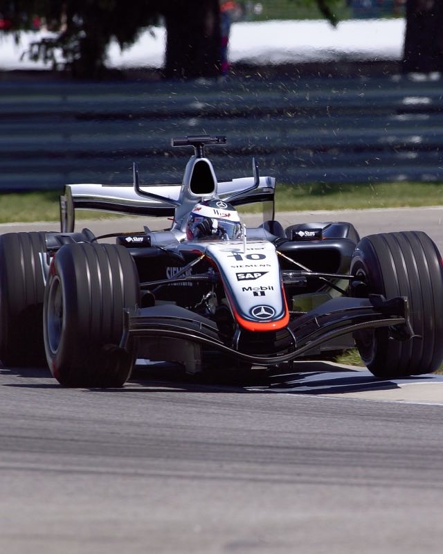A silver McLaren Formula One car numbered 10 turning in on a sunlit racetrack