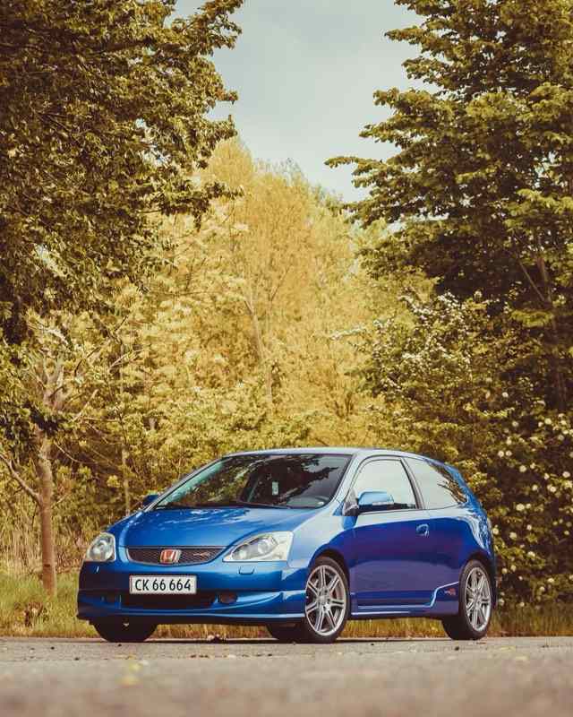 A blue Honda Civic Type R hatchback parked on a road in front of spring trees