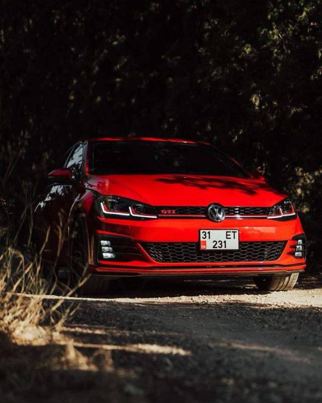 A red Volkswagen Golf GTI parked on a gravel track in dappled woodland light