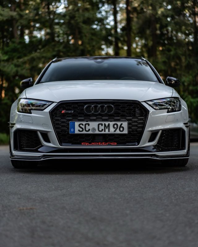 A white Audi RS 3 photographed head-on from low down on a forest road