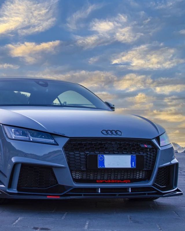 The front of a grey Audi TT RS parked on a seafront at dusk