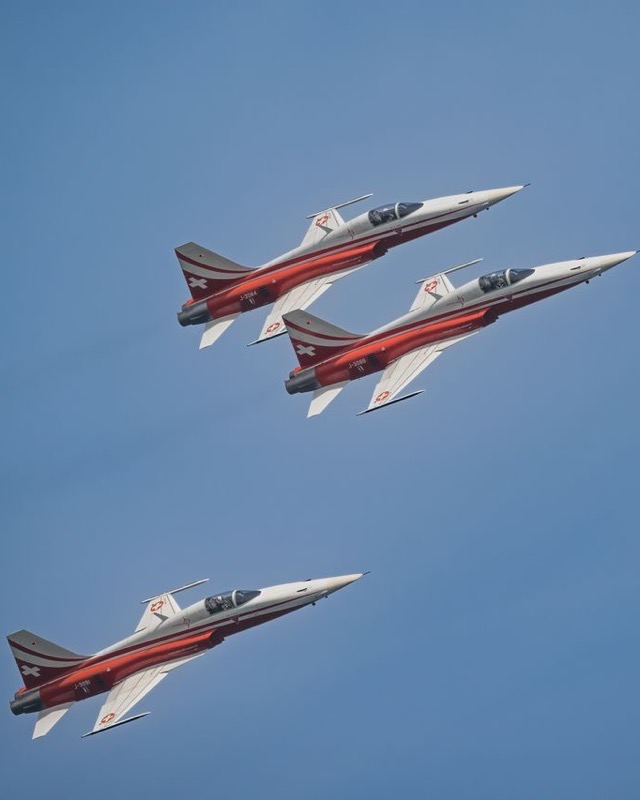 Three red and white Patrouille Suisse F-5E Tiger II fighters banking together against a deep blue sky