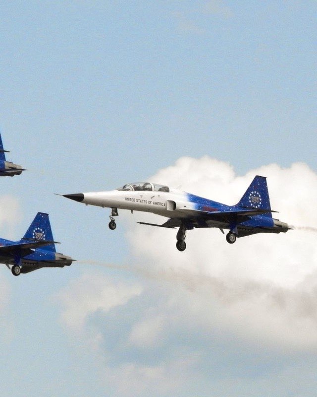 Three United States Air Force T-38 Talon trainers flying in formation with their landing gear down, the nearest one white with a blue star-covered tail
