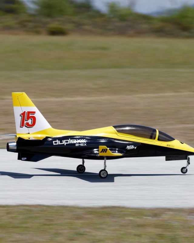 A yellow and black radio-controlled model jet rolling down a runway, its metal tailpipe protruding from the tail