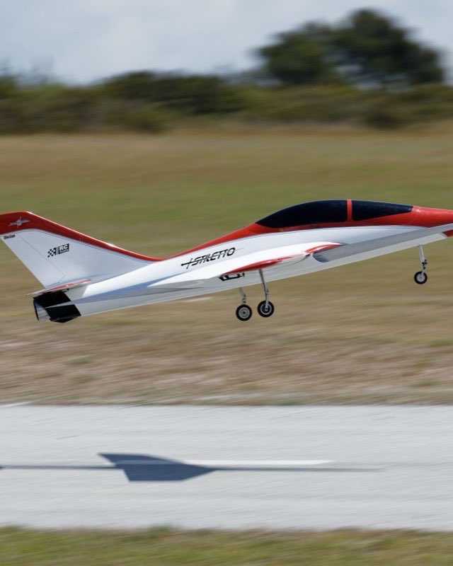 A red and white radio-controlled model jet lifting off a runway with its landing gear still down
