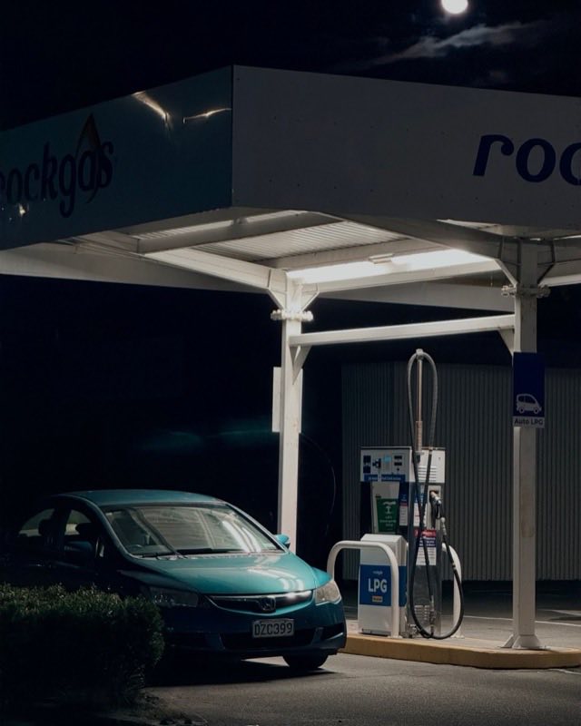 A teal Honda sedan parked beside an Auto LPG dispenser under a lit Rockgas canopy at night, with a full moon overhead