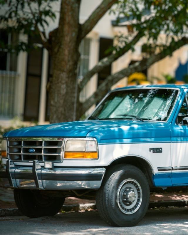 A blue and white Ford F-250 extended cab parked under a tree on a residential street
