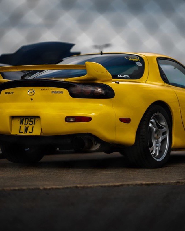 The rear three-quarter of a yellow third-generation Mazda RX-7 parked at a track day