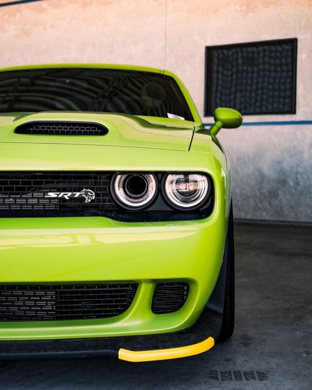 The front corner of a lime green Dodge Challenger SRT Hellcat Widebody parked in a concrete garage