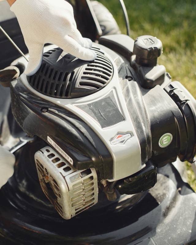 A gloved hand pulling the starter cord of a Briggs and Stratton engine on a walk-behind mower