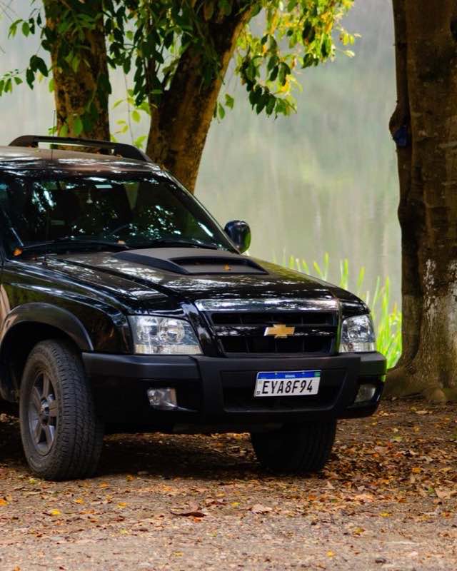 The front of a black Chevrolet S10 crew-cab pickup parked under a tree beside a lake