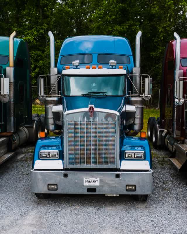 Three Kenworth W900 tractors in green, blue and red parked side by side on gravel