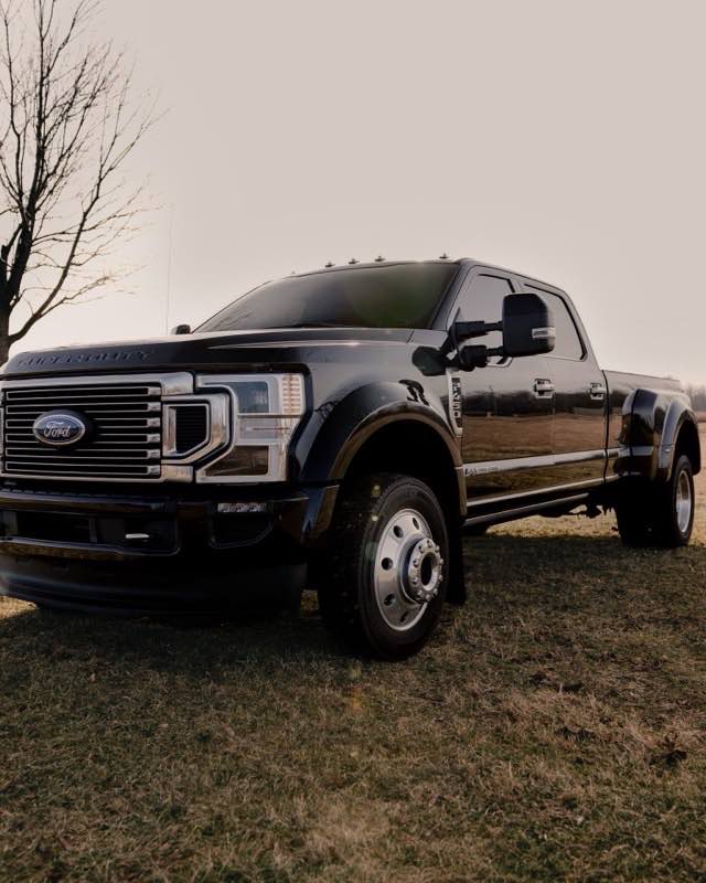 A black Ford Super Duty dual-rear-wheel pickup parked on winter grass beside a bare tree