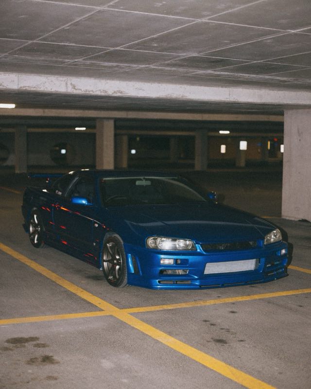 A blue Nissan Skyline GT-R R34 parked in a concrete garage