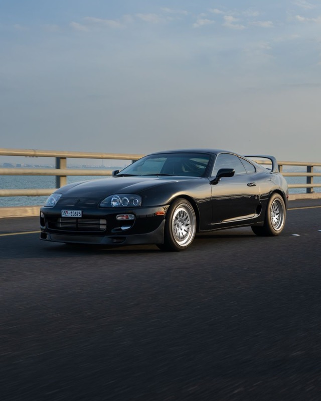 A black fourth-generation Toyota Supra on a coastal bridge at sunset
