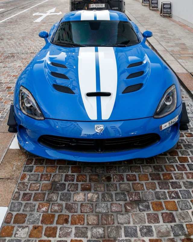 A blue Dodge Viper with white racing stripes seen head-on on a cobblestone street