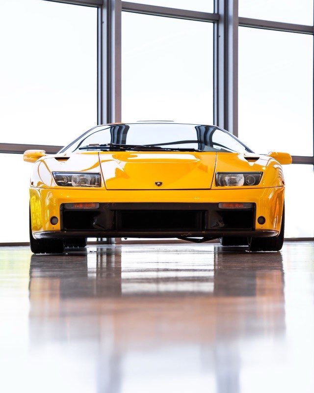 A yellow Lamborghini Diablo photographed head-on in a bright glass-walled showroom
