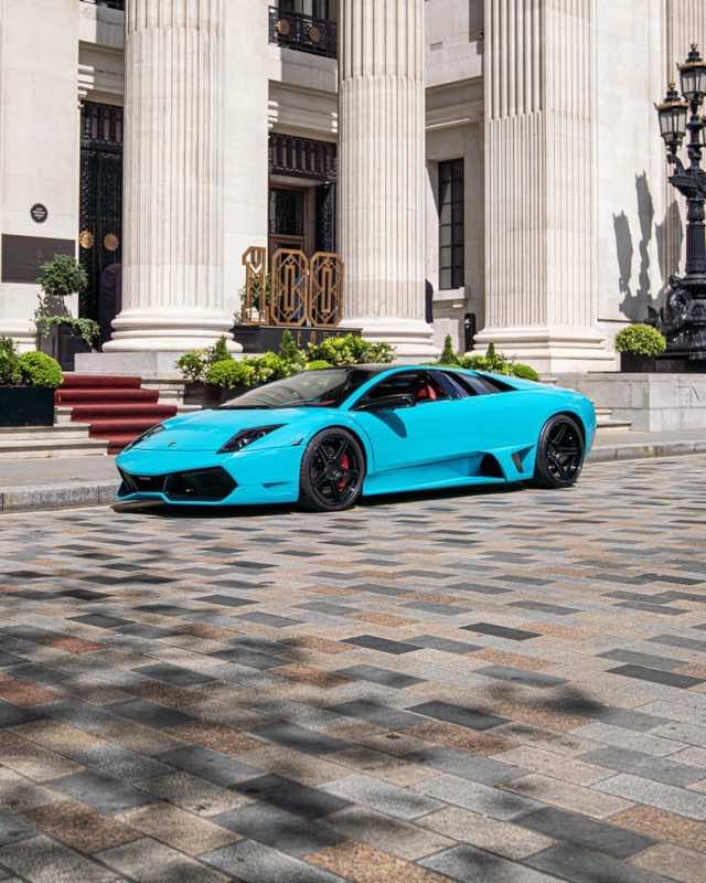 A turquoise Lamborghini Murciélago parked on patterned paving in front of a classical stone colonnade in London