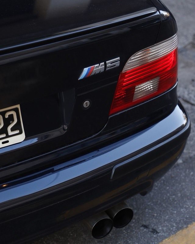 The boot lid of a black BMW E39, an M5 badge beside the taillight and twin round exhaust tips below