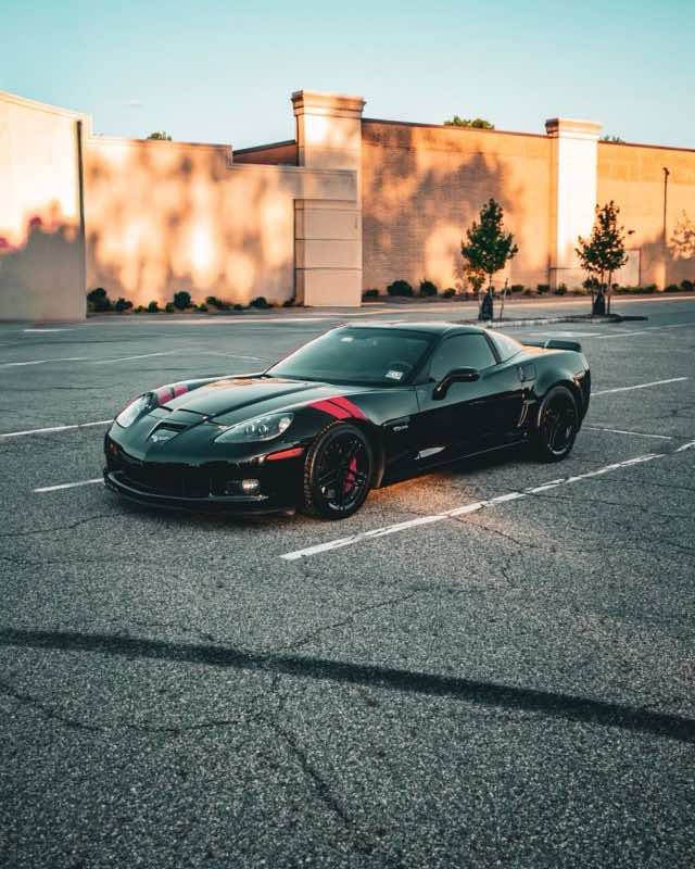 A black Chevrolet Corvette Z06 with red stripes parked in an empty lot at sunset