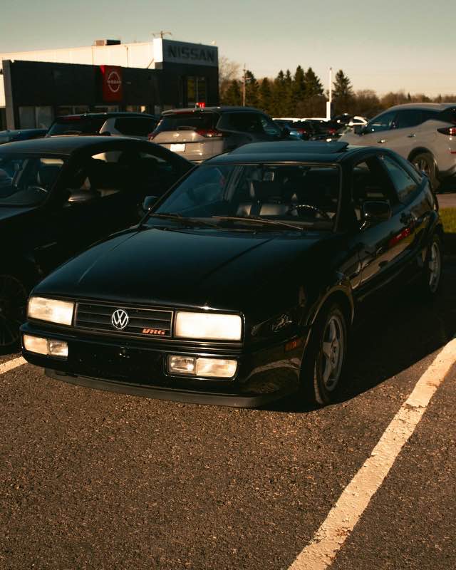 A black Volkswagen Corrado coupe with a red VR6 grille badge, parked in a lot at low sun