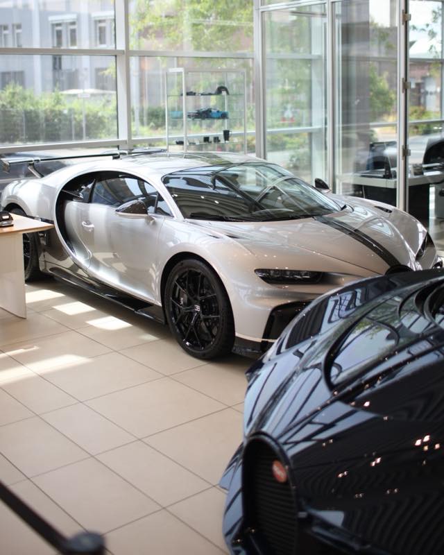 A silver Bugatti Chiron with its door raised in a glass-walled showroom