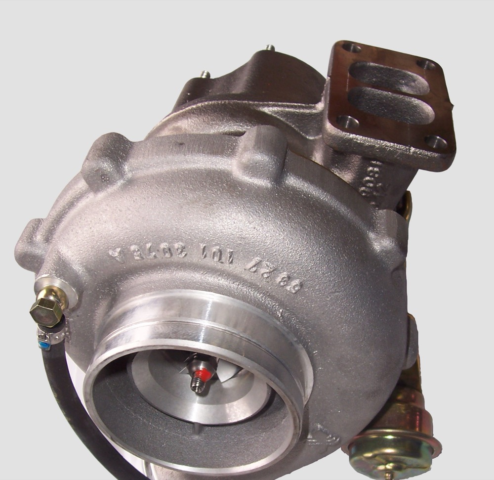 Photograph of a diesel engine turbocharger, showing the cast aluminium compressor housing with the compressor wheel visible inside the inlet, the divided cast-iron turbine inlet flange top right, oil feed and drain lines, and a gold-coloured wastegate actuator canister on the right